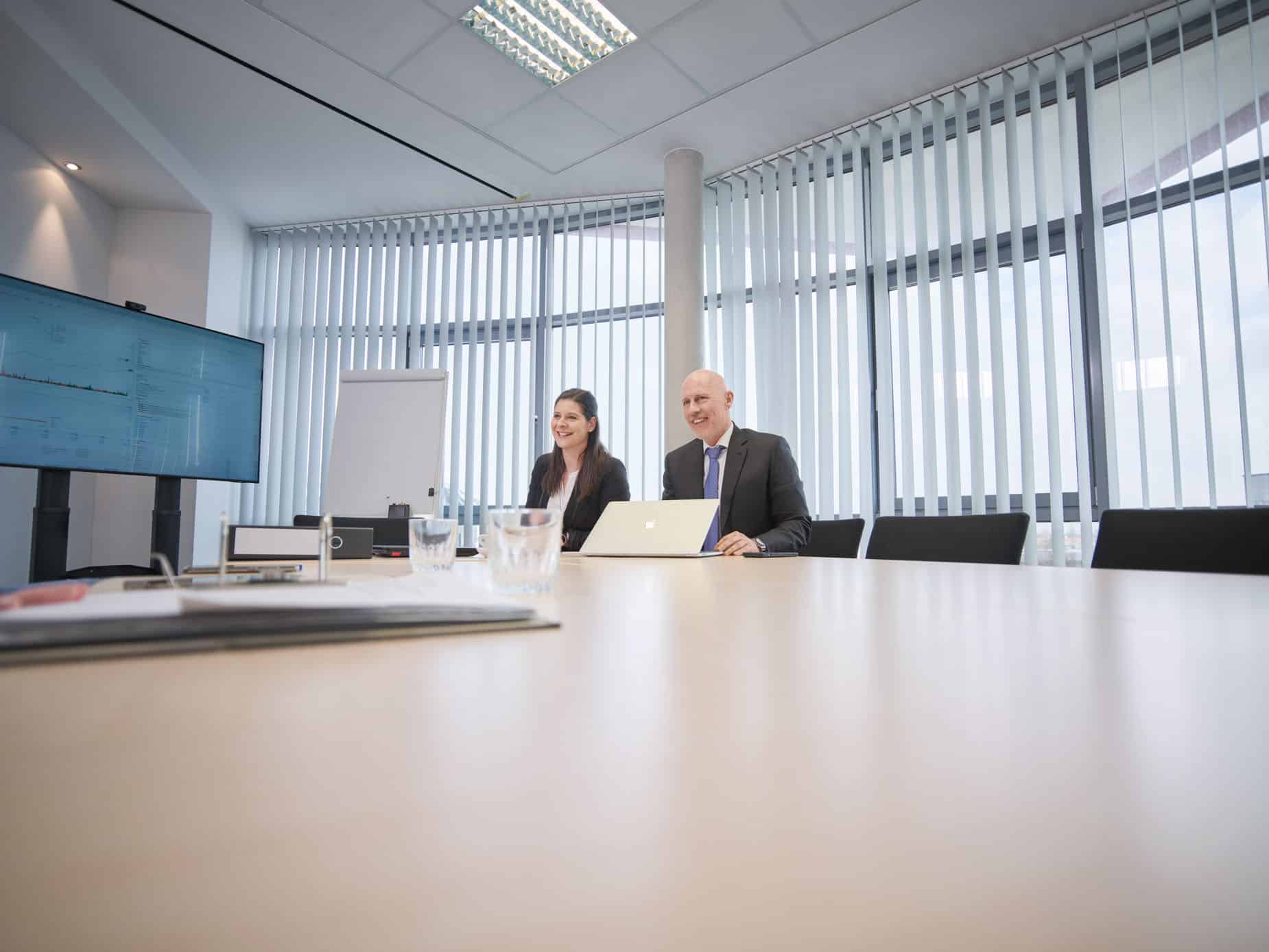 Zwei Geschäftsleute im Büro mit Laptop und Monitoren.